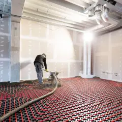 Un ouvrier installe un système de chauffage par le sol électrique, avec des tuyaux rouges sur une grille noire.