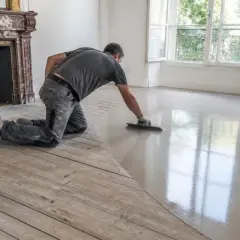 Un ouvrier effectue un ragréage sur plancher bois, créant une surface lisse et moderne.