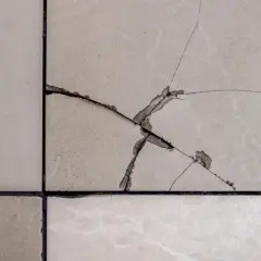 Gros plan sur un carrelage beige avec une fissure traversant plusieurs carreaux, révélant la couche inférieure.