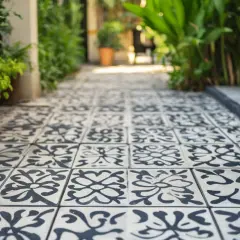 Un chemin bordé de plantes mène à une allée pavée de carreaux de ciment décorés, prêts à être poncés pour révéler leur beauté.