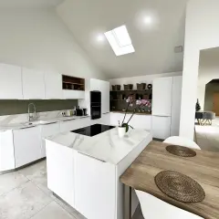 Cuisine moderne avec îlot central en marbre blanc et bois. Éclairage naturel par puits de lumière.