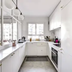 Cuisine en longueur plan, blanche et lumineuse, avec plan de travail en marbre, évier, four et rangements.