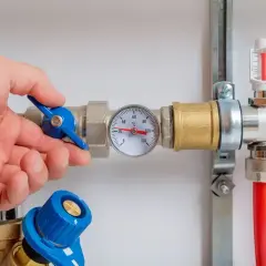 Main d'un homme ajustant la vanne d'un chauffe eau à accumulation. Un thermomètre indique la température.