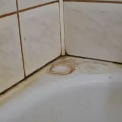 Coins de baignoire sales, avec des traces de javel sur le carrelage et des auréoles sur le blanc.