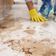 Main jaune nettoyant le carrelage taché, peut-être par de l'acide chlorhydrique.