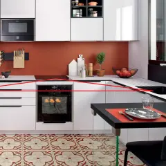 Cuisine moderne avec une organisation optimisée : tiroirs blancs, four encastré, crédence orange, et un îlot noir pour les repas.