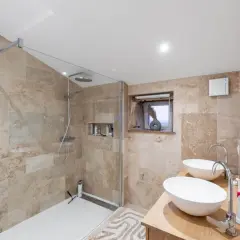 Salle de bain moderne avec douche à l'italienne, double vasque et carrelage en travertin. Une transformation réussie de rénovation salle de bain avant/après.