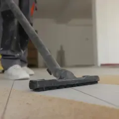 Un ouvrier utilise un aspirateur pour nettoyer le carrelage après le jointoiement. La poussière et les débris sont aspirés.