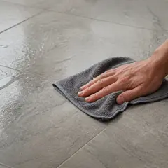 Main tenant nettoie un carrelage poreux avec un chiffon. Le vinaigre blanc est idéal pour ce type de surface.
