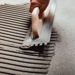 Application d'enduit pour carrelage collé avec une truelle crantée. Les sillons réguliers préparent la surface pour une pose parfaite.