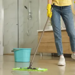 Nettoyer carrelage après chantier : une personne en gants jaunes passe la serpillière sur un sol brillant dans une salle de bain moderne.