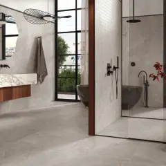 Salle de bain moderne avec baignoire îlot, douche vitrée et lavabo suspendu. La faïence grise habille les murs et le sol, créant une ambiance épurée et luxueuse.