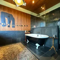 Salle de bain moderne avec baignoire sur pieds noire, tapis persan et mur boisé orné d'une œuvre d'art abstraite. Une **rénovation baignoire** réussie.