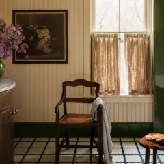 Ambiance de salle de bain rustique avec un lavabo en marbre, des lilas violets, un tableau ancien et une chaise en bois.