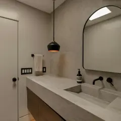 Élégante salle de bain avec un lavabo en **béton ciré** intégré, un miroir arqué et un éclairage moderne.