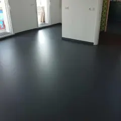 Un sol en résine époxy noir brillant, fraîchement posé, reflète la lumière dans un intérieur moderne.