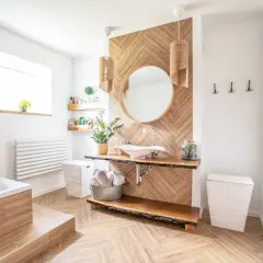 Salle de bain moderne avec sol et murs en bois, baignoire, lavabo et miroir. On peut mettre du parquet dans une salle de bain si le matériau est adapté.