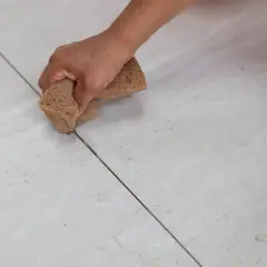 Main d'une personne nettoyant le joint carrelage avec une éponge.