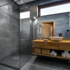 Salle de bain moderne avec douche à l'italienne, carrelage gris, meuble en bois, vasque et miroir. L'étanchéité de la douche italienne est assurée par un receveur discret.