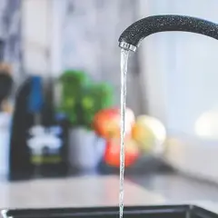 Un robinet moderne coule dans une cuisine. Un préparateur ECS discret est visible à l'arrière-plan, à côté d'un distributeur de savon.
