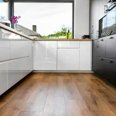 Cuisine moderne avec des armoires blanches et noires brillantes, un grand évier et un parquet au sol chaleureux.