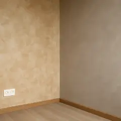 Coin de mur avec une peinture effet taloche beige clair et une autre murale gris taupe. Plinthe en bois et prise électrique blanche.