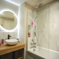 Salle de bain sans fenêtre, lumineuse avec un grand miroir rond éclairé, une vasque moderne et une douche à l'italienne.