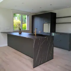 Îlot de cuisine moderne avec plan de travail en marbre noir veiné d'or. Ce modèle de cuisine simple, aux lignes épurées, est complété par des meubles sombres et un robinet doré.