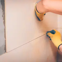 Pose de carreaux : une main gantée ajuste le **taille joint carrelage** pour une finition parfaite.