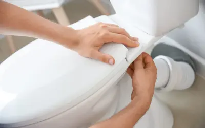 Mains ajustant le siège d'un WC. La hauteur de l'alimentation en eau du WC est correcte.