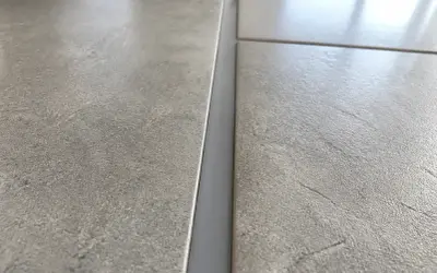 Gros plan sur un joint de dilatation carrelage gris, entre deux carreaux texturés.