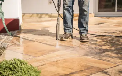 Un homme nettoie un carrelage antidérapant avec un nettoyeur haute pression. L'eau éclabousse sur les dalles.