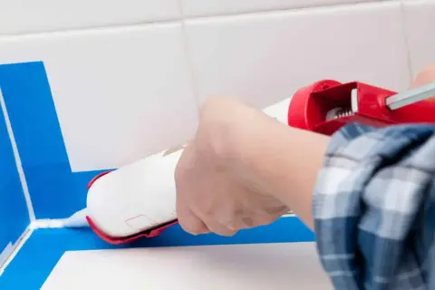Application d'un joint silicone blanc avec un pistolet pour assurer l'étanchéité de la douche. Le bon quel joint pour douche est essentiel.