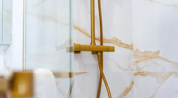 Robinet de douche doré, avec un pommeau réglable en hauteur, sur un mur carrelé de marbre blanc et or.