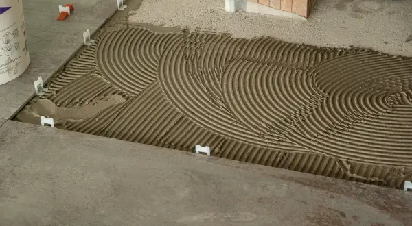 Pose de carrelage : la chape maigre attend les carreaux, avec des croisillons blancs et un lit de colle strié.