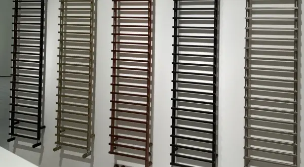 Cinq sèche-serviettes de différentes couleurs (noir, bronze, marron, noir, gris) sont alignés. La hauteur de ces sèche-serviettes est impressionnante.
