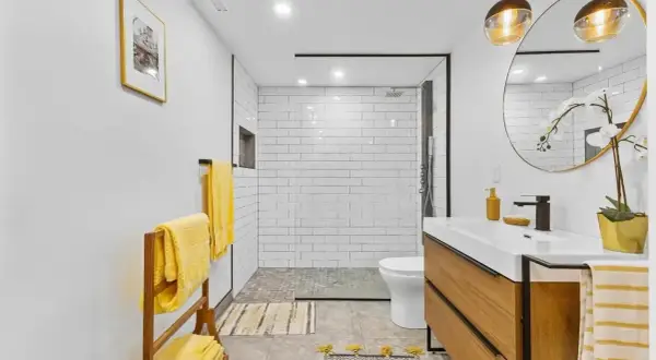 Salle de bain en longueur moderne avec douche carrelée, vasque en bois et serviettes jaunes vives.