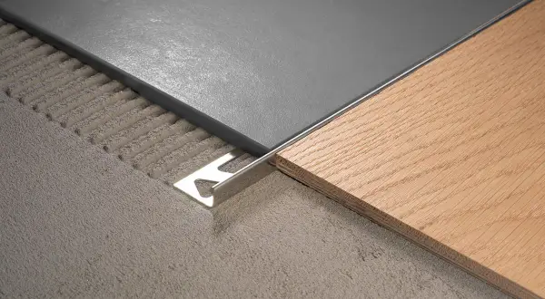 Détail d'un raccord de sol entre carrelage gris et parquet bois, avec une plinthe métallique.