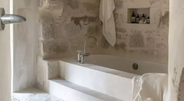 Bain relaxant dans une **salle de bain méditerranéenne** aux murs de pierre brute. Serviette blanche suspendue, robinetterie moderne.
