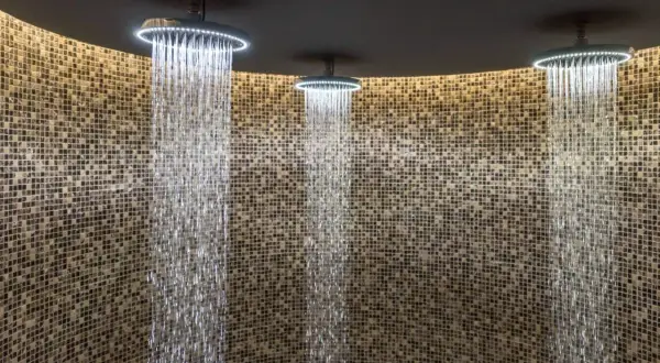 Trois douches modernes avec éclairage LED diffusent des cascades d'eau sur un mur de mosaïque. Une expérience de douche sensorielle unique.