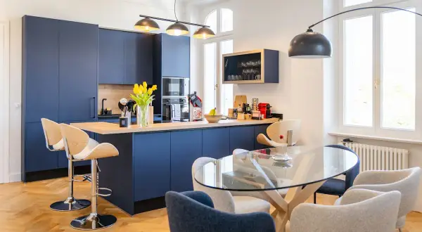 Une belle idée cuisine ouverte sur salon avec des meubles bleus profonds, un îlot central et une table en verre.