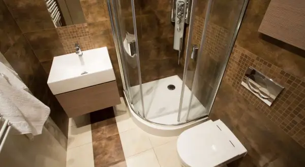 Salle de bain rouille et bois : douche d'angle, lavabo suspendu, toilettes. Ambiance chaleureuse et moderne.