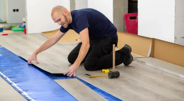 Pose d'un revêtement de sol stratifié sur une sous-couche bleue, assurant une isolation phonique sous carrelage. Outils de pose à proximité.