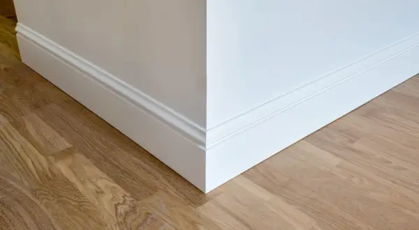 Coin de mur blanc avec plinthe moulurée et parquet en bois clair. La hauteur de la plinthe carrelage est bien visible.