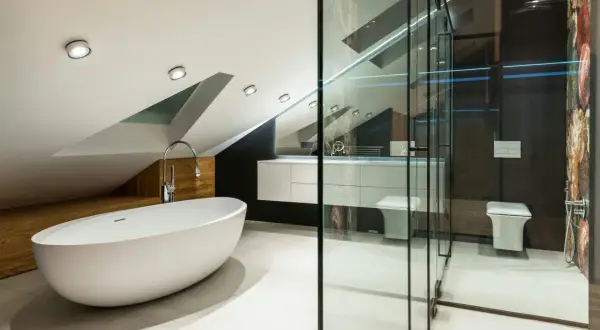 Élégante petite salle de bain mansardée avec baignoire îlot, douche vitrée, lavabo suspendu et WC.