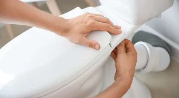 Mains ajustant le siège d'un WC. La hauteur de l'alimentation en eau du WC est correcte.