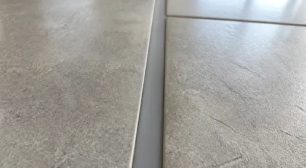 Gros plan sur un joint de dilatation carrelage gris, entre deux carreaux texturés.