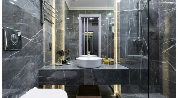 Une **salle de bain de rêve** aux murs de marbre gris, avec vasque ronde, douche moderne et éclairage d'ambiance.