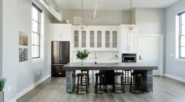Cuisine moderne avec îlot central, tabourets et armoires blanches. Une cuisine sans hotte, avec un style épuré et industriel.
