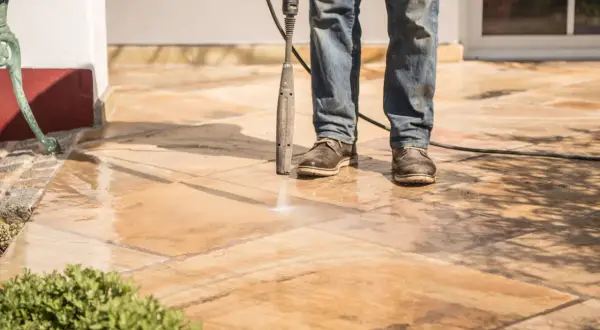 Un homme nettoie un carrelage antidérapant avec un nettoyeur haute pression. L'eau éclabousse sur les dalles.